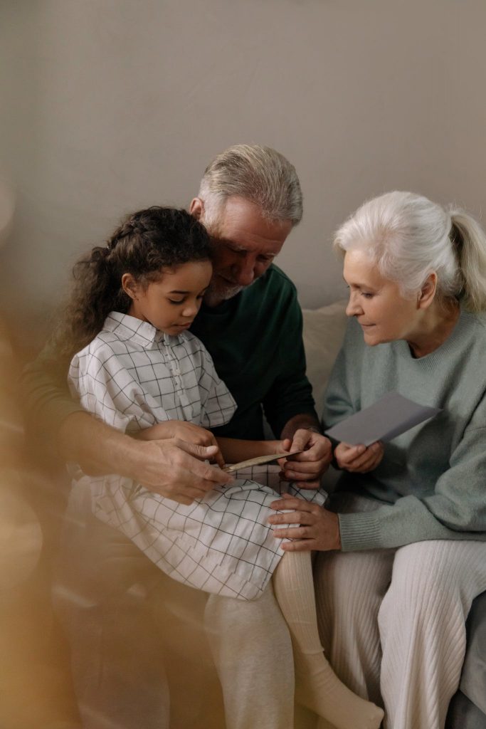 Grandparents and a Girl Sitting on a Couch while Reading a Book